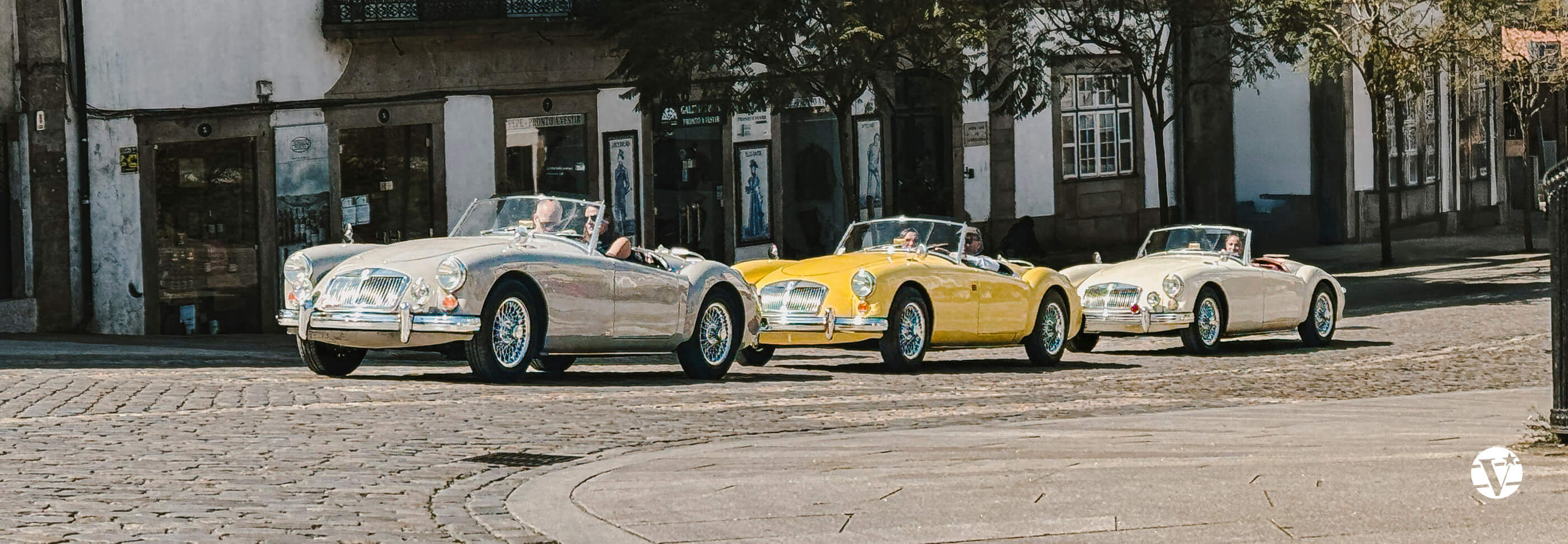 MGA Roadster fahren bei strahlendem Sonnenschein durch das historische Zentrum von Ponte de Lima, vorbei an alten Häusern.